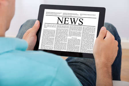 Closeup of mid adult man reading newspaper on digital tablet at homeの写真素材