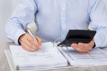 Midsection of businessman calculating financial expenses at deskの写真素材