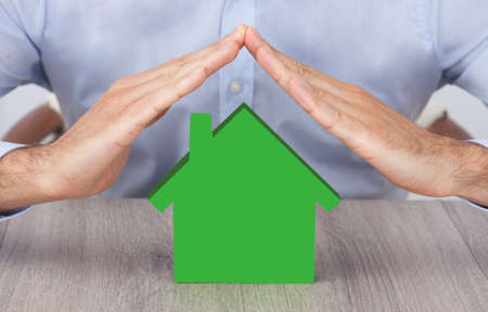 Midsection of businessman's hands over green model house at deskの写真素材