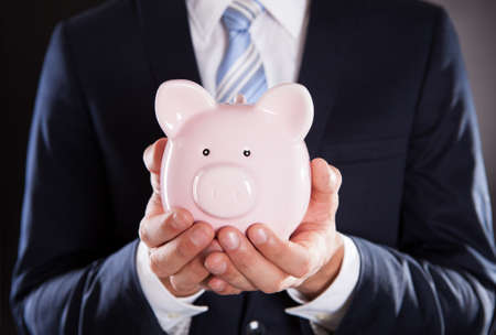 Midsection of businessman holding piggybank against black backgroundの写真素材