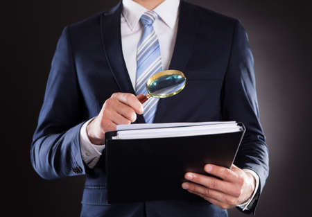 Midsection of businessman examining documents with magnifying glass against black backgroundの写真素材
