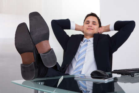 Full length of relaxed businessman daydreaming in officeの写真素材