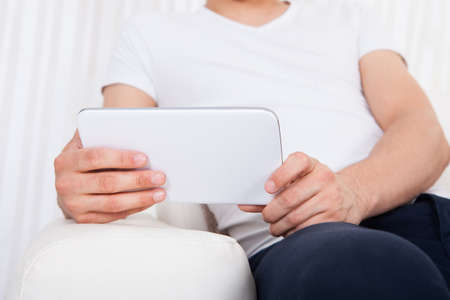 Cropped image of young man using digital tablet in living room
