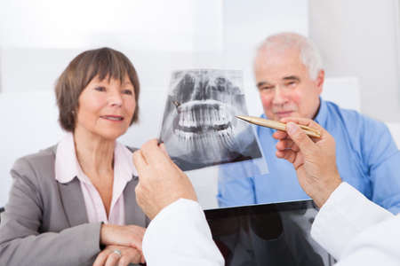Male dentist explaining dental x-ray to senior couple in clinicの写真素材