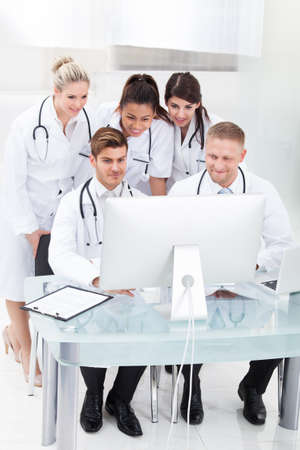 Team of doctors using desktop PC together at desk in clinicの写真素材