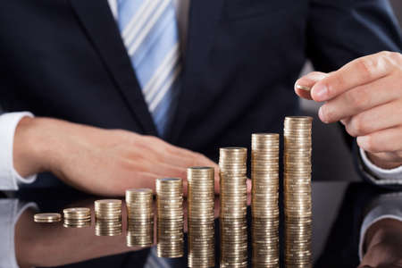 Midsection of businessman stacking coins at deskの写真素材