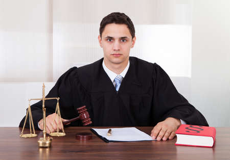 Portrait of confident male judge sitting at table in courtroom