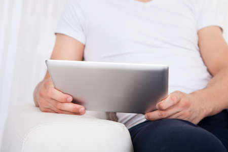 Cropped image of young man using digital tablet in living room