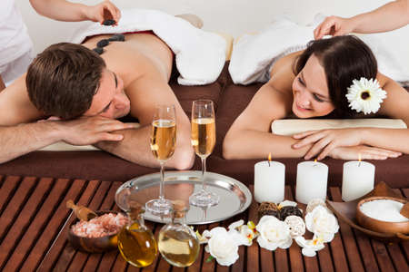 Smiling young couple enjoying hot stone massage at beauty spaの写真素材