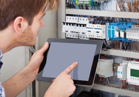 Side view of male technician examining fusebox while holding tabletの写真素材