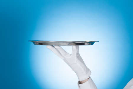Cropped image of waiter carrying empty tray over blue backgroundの写真素材