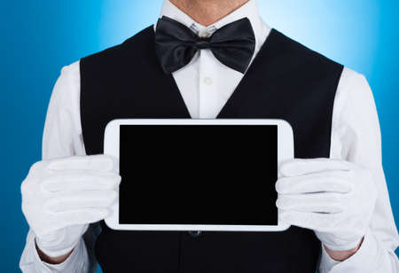 Midsection of waiter showing digital tablet over blue backgroundの写真素材