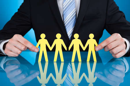 Midsection of businessman's hands holding paper people chain on desk against black backgroundの写真素材