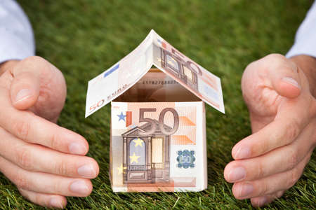 Businessman's hands protecting house made of euro notes on grassy landの写真素材
