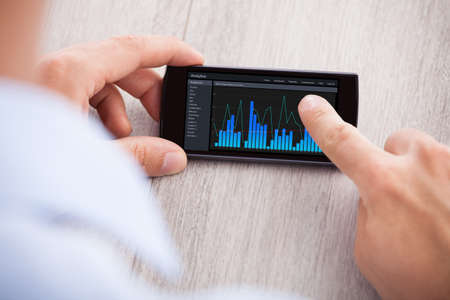 Cropped image of businessman analyzing graph on smartphone at desk in office