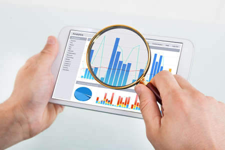 Cropped image of businessman examining graph on digital tablet with magnifying glass at office deskの写真素材
