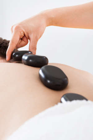 Midsection of female therapist placing hot stones on man's back in spa