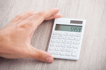 Closeup of businessman's hand holding calculator on deskの写真素材