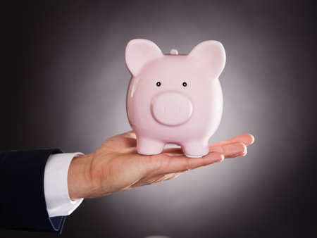 Cropped image of businessman holding piggybank over black backgroundの写真素材