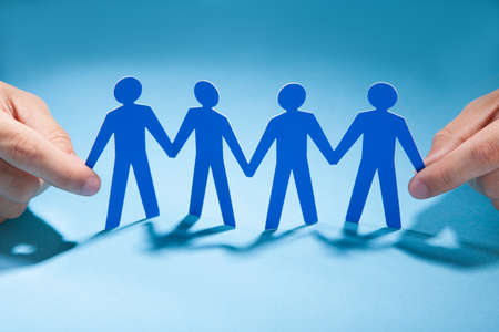 Cropped image of businessman's hands holding paper people chain on deskの写真素材