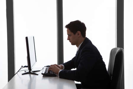 Side view of young businessman using computer at desk in officeの写真素材