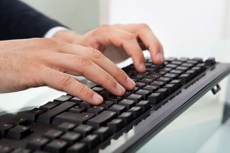 Cropped image of businessman using computer keyboard at desk in officeの写真素材