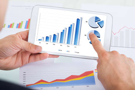 Cropped image of businessman comparing graphs on digital tablet at desk in office