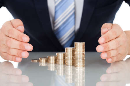 Midsection of businessman's hand protecting coins at desk against black backgroundの写真素材