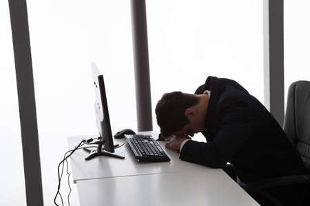 Side view of tired young businessman sleeping at computer desk in officeの写真素材