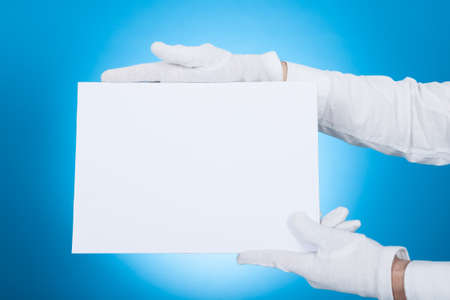 Cropped image of butler holding blank placard over blue backgroundの写真素材