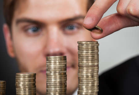 Young businessman stacking coins at desk against black backgroundの写真素材