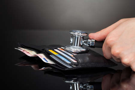 Cropped of man's hand examining wallet with stethoscope at desk against black background