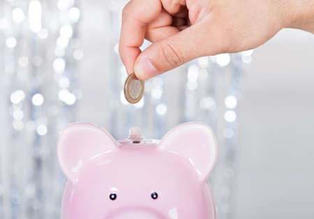 Cropped image of man inserting coin in piggybank indoorsの写真素材