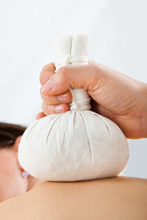 Closeup of young woman receiving massage with herbal compress bags on back at spaの写真素材