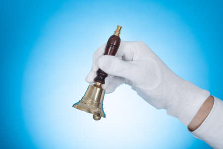 Cropped image of butler holding call bell over blue background