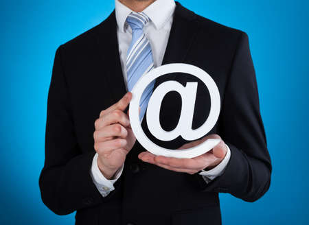 Midsection of young businessman holding at symbol against blue backgroundの写真素材