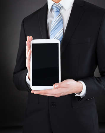 Midsection of businessman showing digital tablet against black backgroundの写真素材