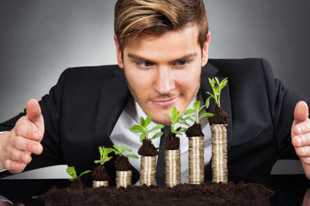 Young businessman protecting coins in saplings representing responsible business against black backgroundの写真素材