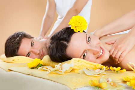 Portrait of smiling young woman receiving shoulder massage with man in background at spaの写真素材