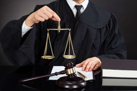Midsection of male judge holding weight scale at desk against black backgroundの写真素材