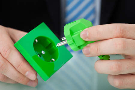 Cropped image of businessman holding green electric plug and socket at office deskの写真素材