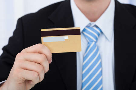 Midsection of businessman holding credit card in officeの写真素材