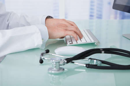 Midsection of young male doctor using computer at desk in clinic