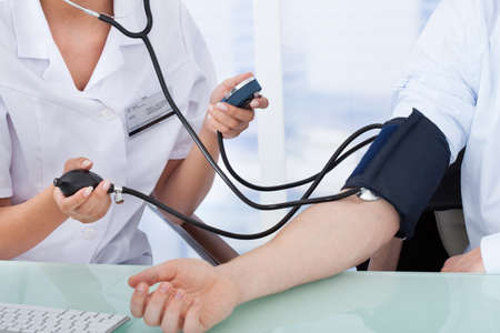 Cropped image of young female doctor checking blood pressure of businessman in clinic