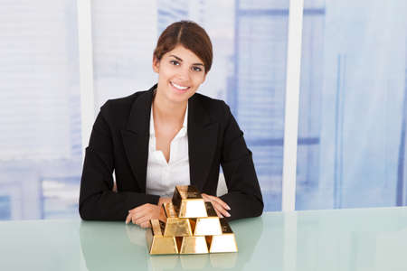 Portrait of confident businesswoman showing stacked gold blocks on desk in officeの写真素材