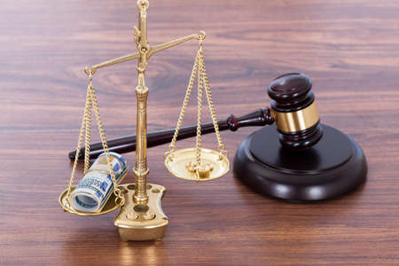 Judge gavel and scales with money on wooden deskの写真素材