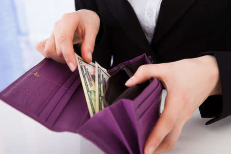Midsection of businesswoman putting American banknotes in wallet at office deskの写真素材