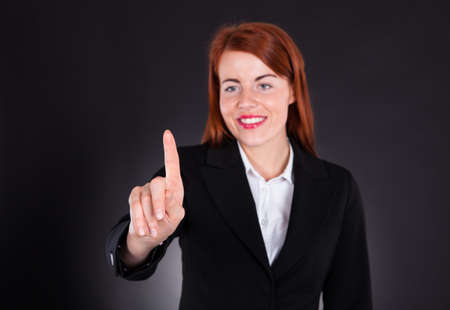 Happy young businesswoman touching imaginary screen against black backgroundの写真素材