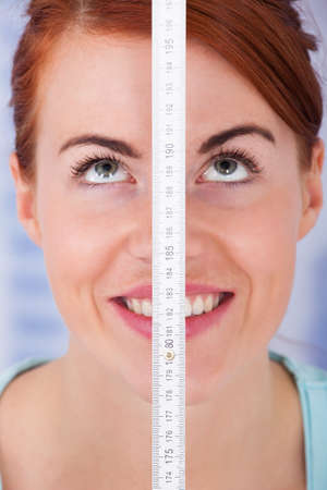 Closeup of beautiful young woman measuring height with measure tapeの写真素材