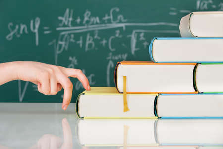 Cropped image of woman's hand climbing stack books in classroomの写真素材
